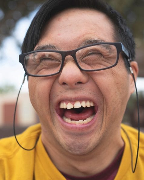A headshot of a person with Down syndrome wearing glasses and smiling.