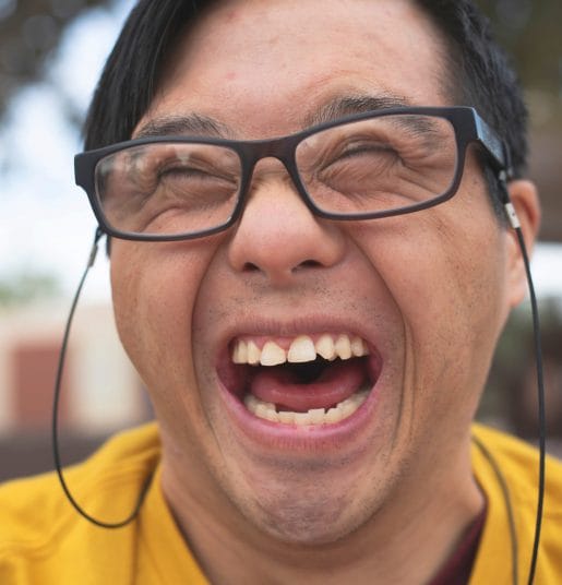 A headshot of a person with Down syndrome wearing glasses and smiling.