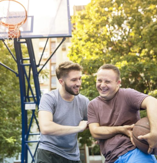 Two young men smiling playing basketball.