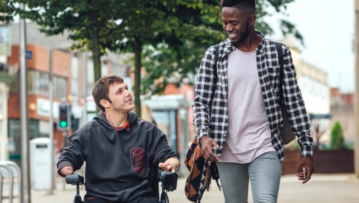 A young man walking besides a person in a wheelchair.