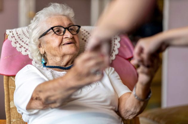 An elderly person grabbing for someone's hands.