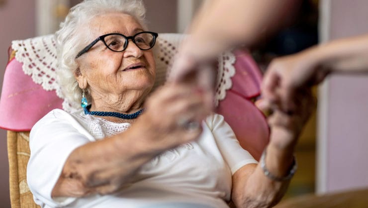 An elderly person grabbing for someone's hands.