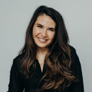 A smiling woman with long brown hair in a black collared shirt.