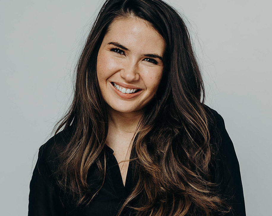 A smiling woman with long brown hair in a black collared shirt.