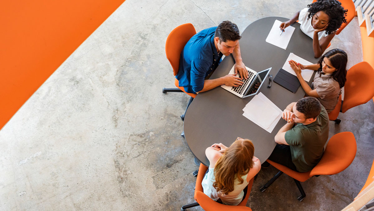 An overhead photo of 5 people working around a table in an office.
