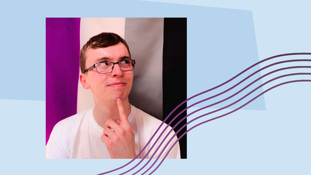 A photo of Liam O’Dell pointing to his chin in front of the Ace Pride flag.
