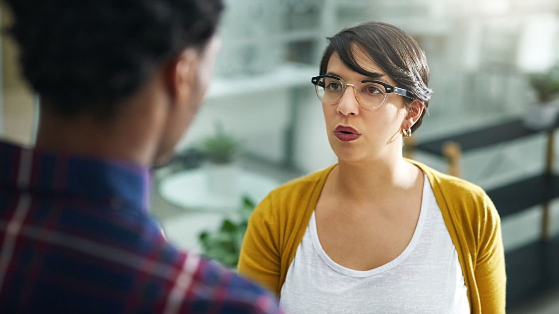 A woman with short hair and glasses has a conversation with another person.