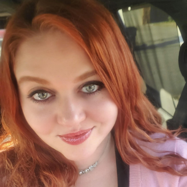 Portrait of Stefanie Porter, a woman smiling with shoulder-length red hair and a pink sweater.