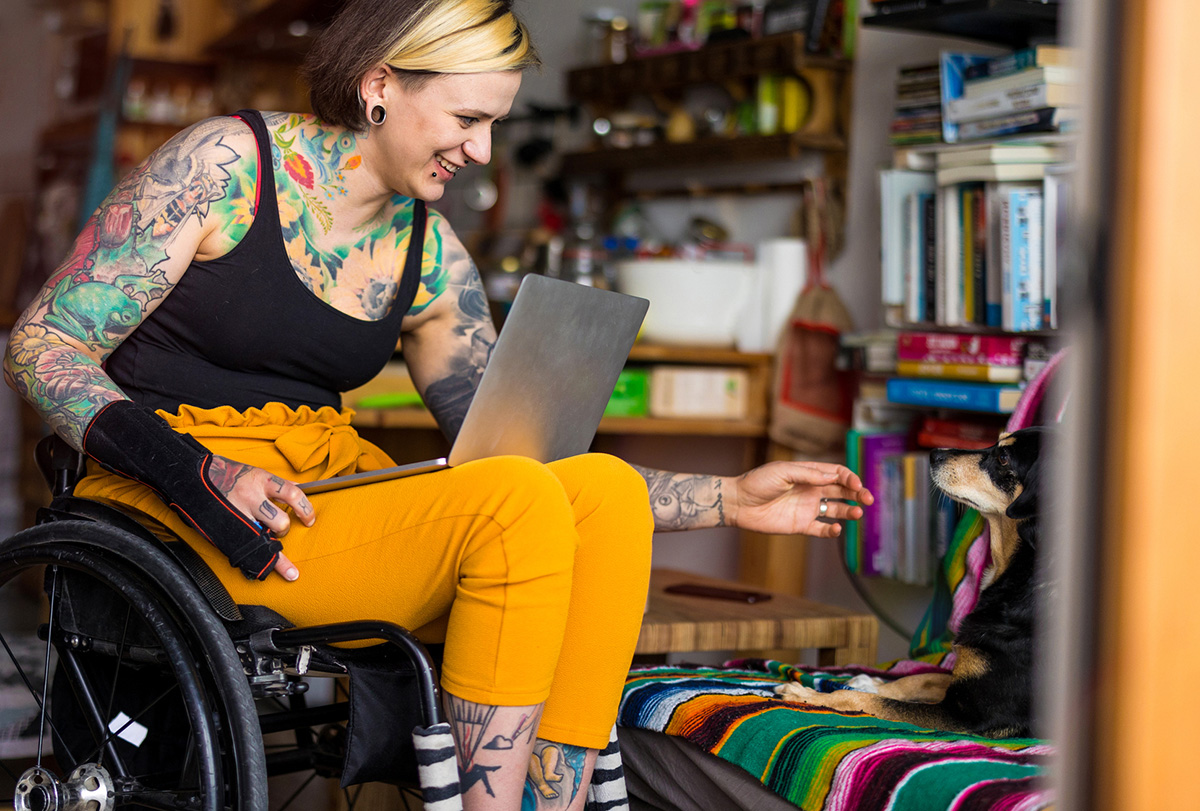 A woman in a wheelchair reaches her hand out to a dog.