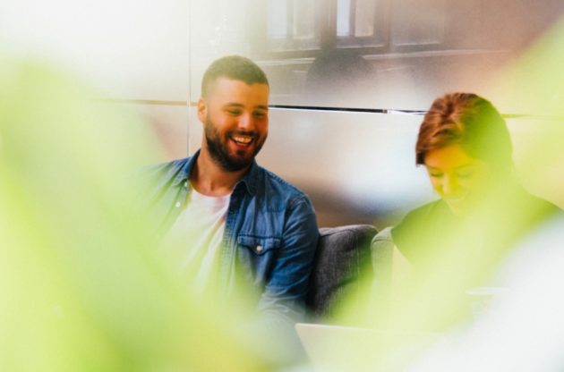 Two people collaborating at work with a green plant in the foreground.