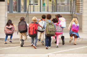 A group of young children with only backs visibile with backpacks at school.