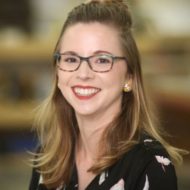 A professional headshot of Sierra Smith with long, light brown hair, wearing glasses and a black floral blouse.