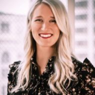 Portrait of Emily Hanson, a smiling woman with long blonde hair, wearing a patterned blouse, against a light background.